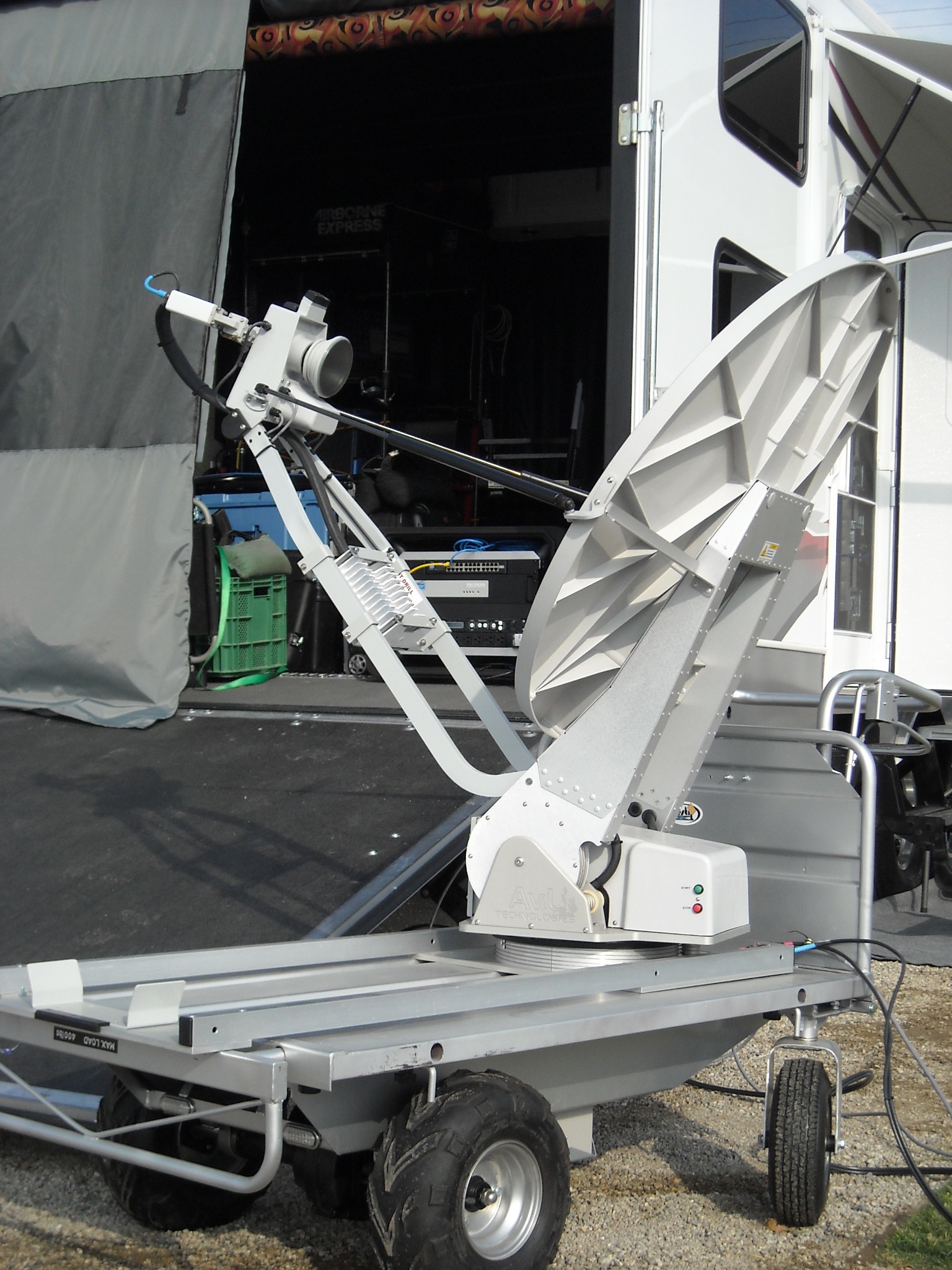Close view of a mobile satellite dish, rover cart and broadcast equipment beside a production truck