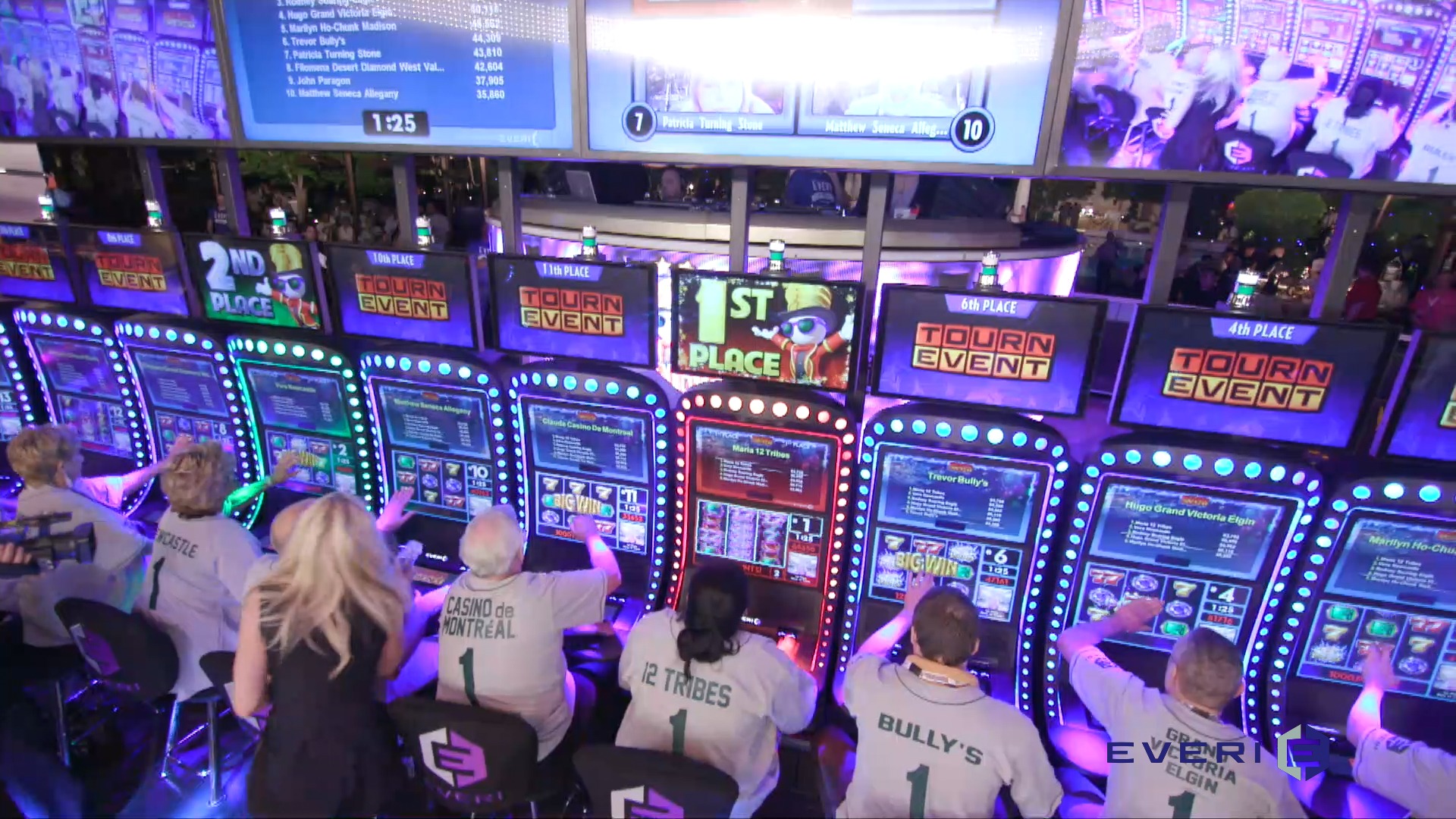 Slot tournament competitors beneath live camera feeds and leaderboards, with illuminated tournament machines